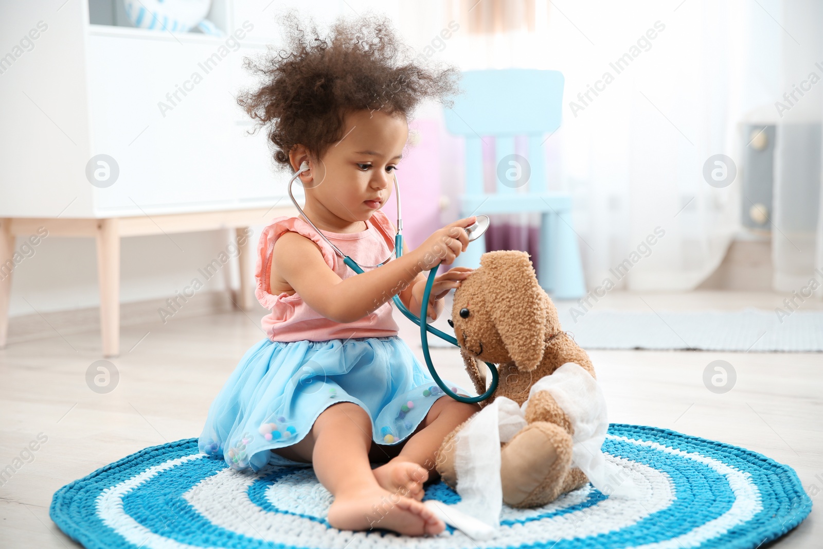 Photo of Cute African American child imagining herself as doctor while playing with stethoscope and toy bunny at home