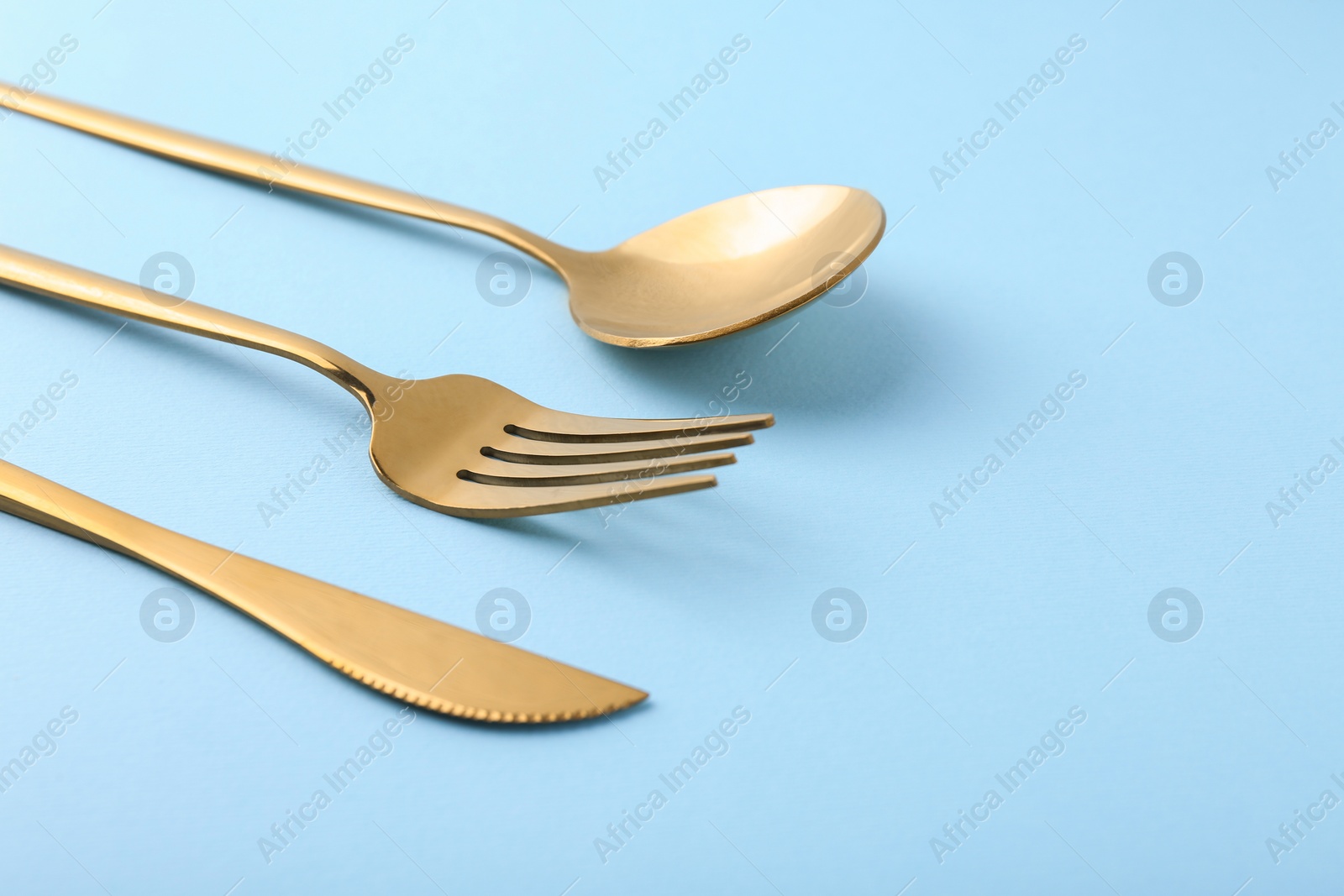 Photo of Stylish golden cutlery set on light blue background, closeup. Space for text