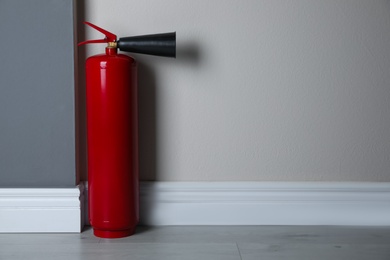 Photo of Fire extinguisher near light wall indoors. Space for text