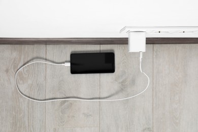 Modern smartphone charging from electric socket indoors, top view