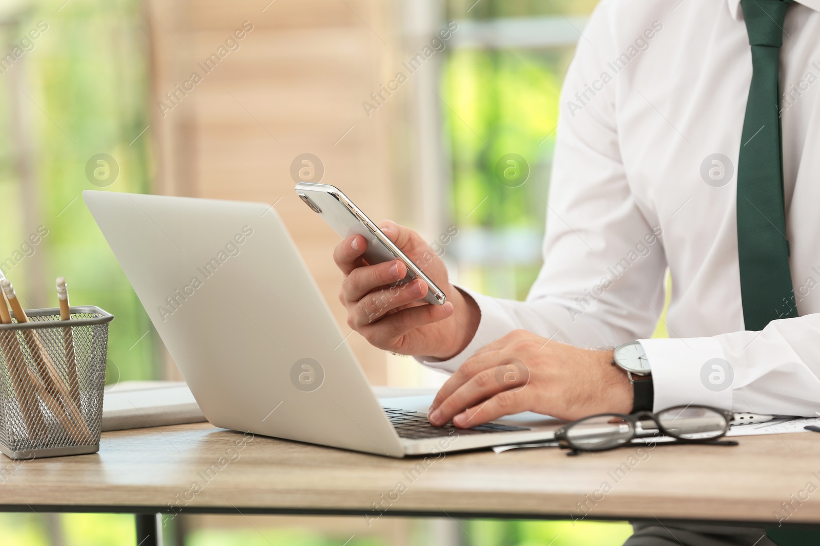 Photo of Young man working with laptop and mobile phone at table, closeup