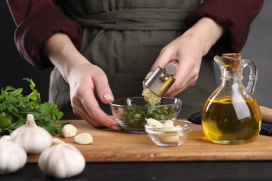 Photo of Woman squeezing garlic with press at black table, closeup
