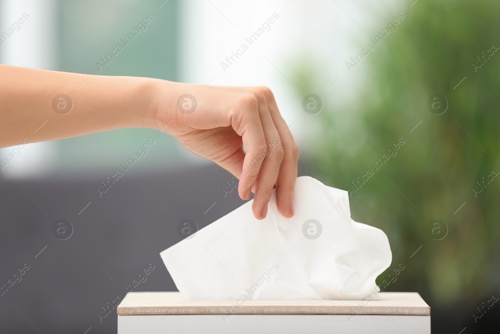 Photo of Woman taking paper tissue from holder on blurred background, closeup