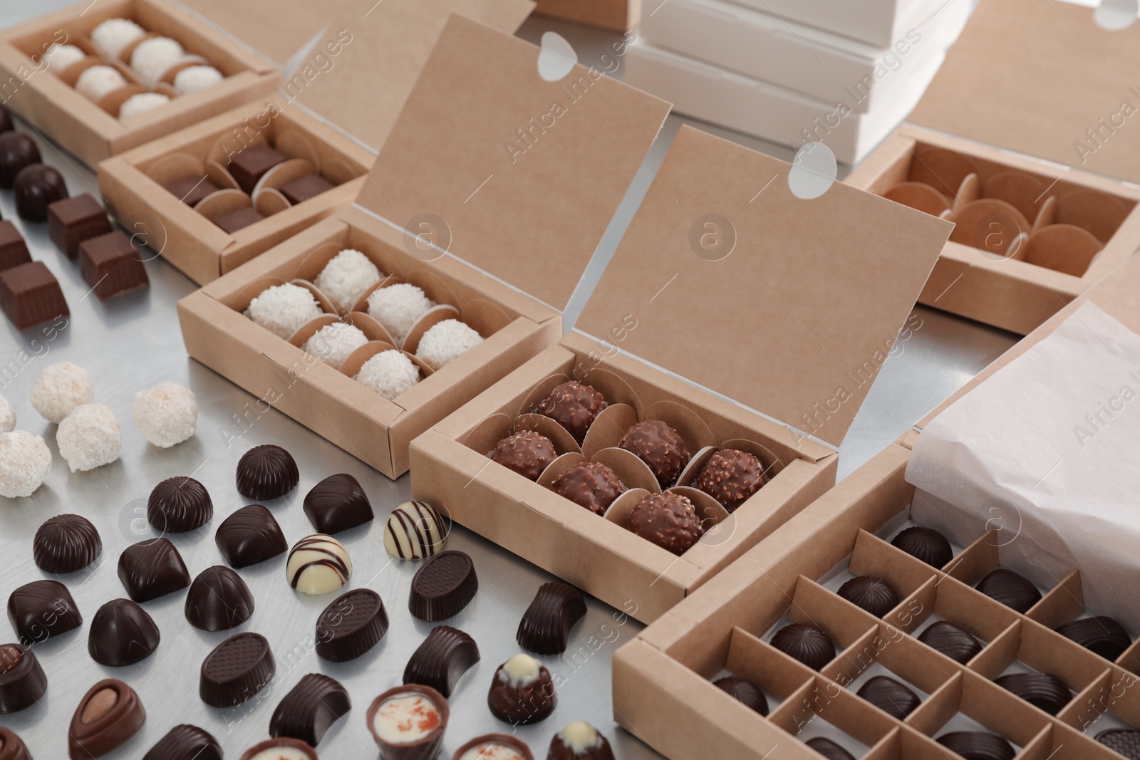 Photo of Different delicious chocolate candies and boxes on white table. Production line