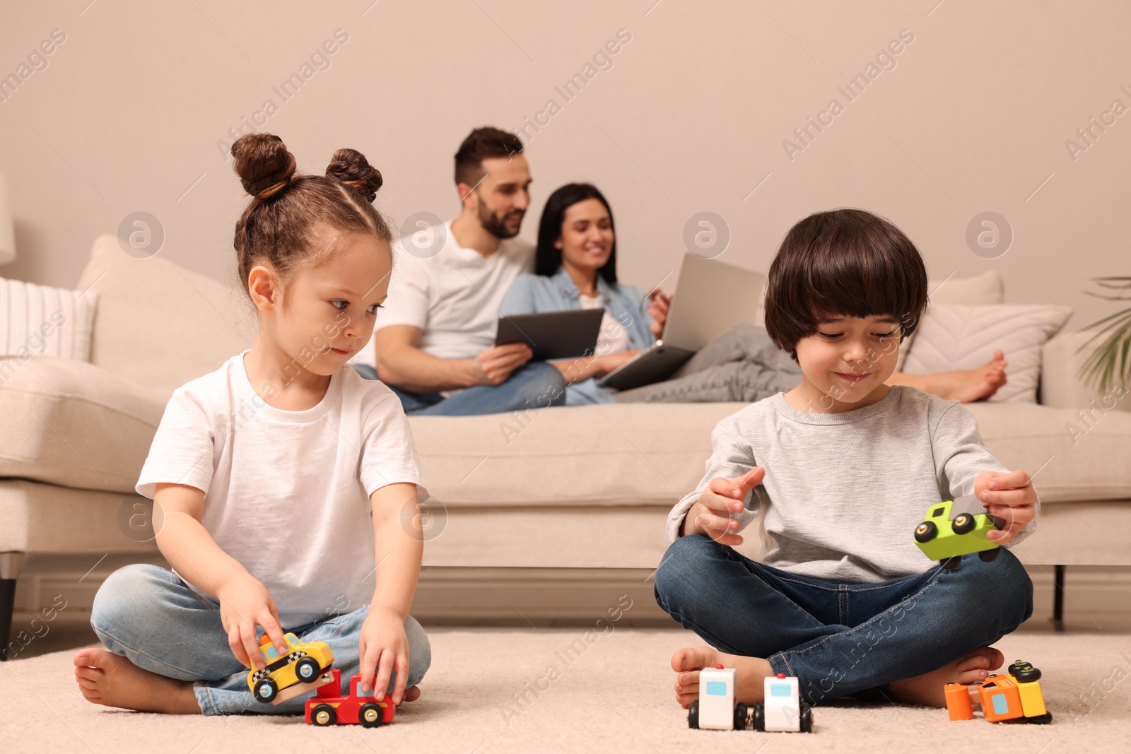 Photo of Cute children playing with toys while parents using gadgets on sofa in living room