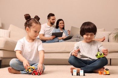 Photo of Cute children playing with toys while parents using gadgets on sofa in living room
