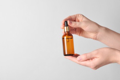 Photo of Woman holding bottle of cosmetic oil on light background, closeup. Space for text