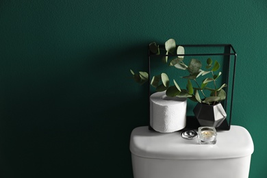 Photo of Decor elements and paper roll on toilet tank near green wall, space for text. Bathroom interior