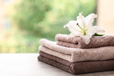 Photo of Stack of clean towels with lily on table against blurred background. Space for text