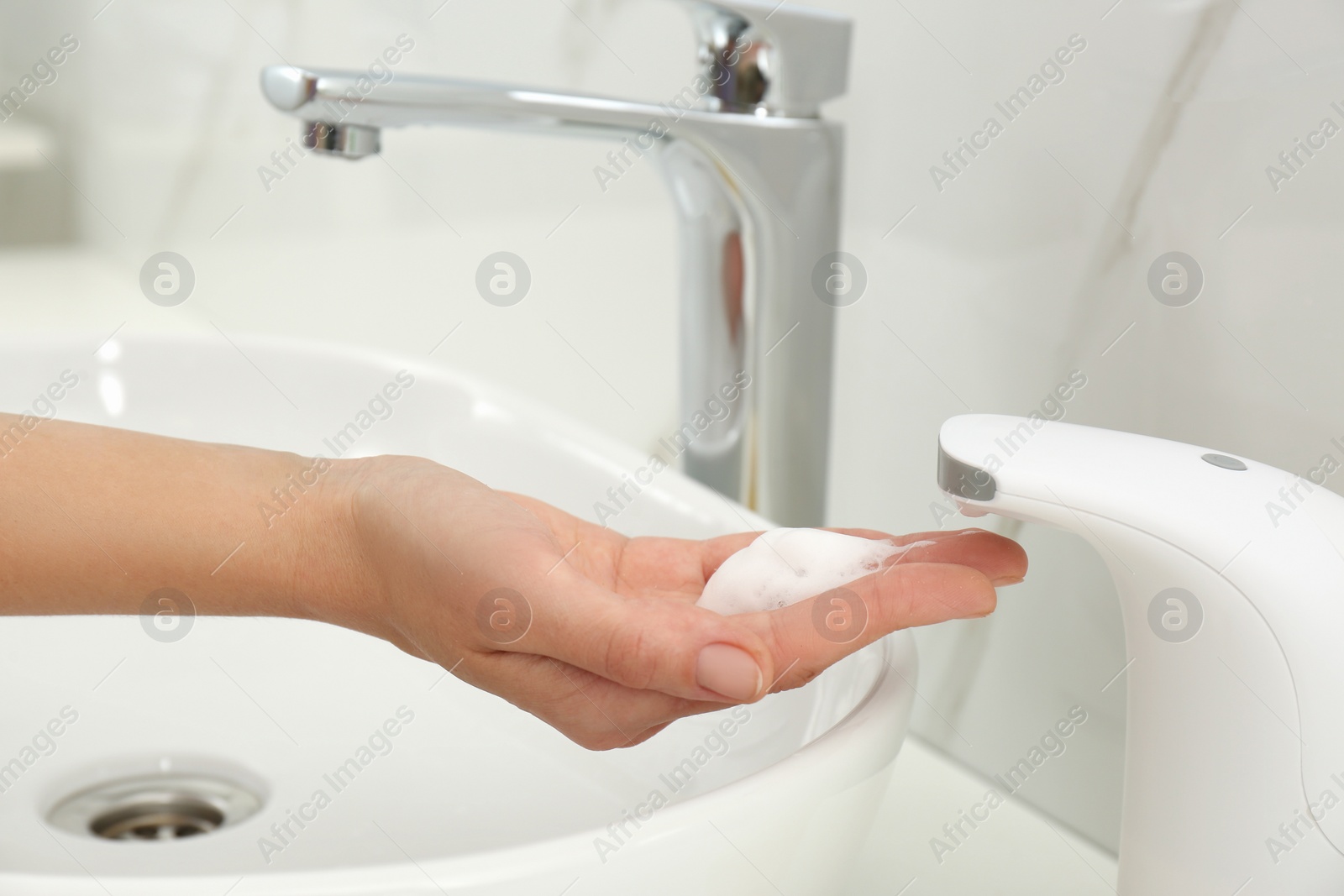 Photo of Woman using automatic soap dispenser in bathroom, closeup