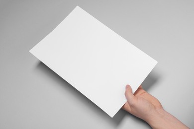 Photo of Woman holding sheet of paper on light grey background, closeup. Mockup for design