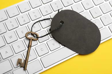 Photo of Vintage key with blank tag and keyboard on yellow background, closeup. Keyword concept