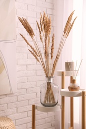 Photo of Fluffy reed plumes near white brick wall indoors. Interior element