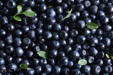 Photo of Many delicious ripe bilberries and green leaves as background, top view