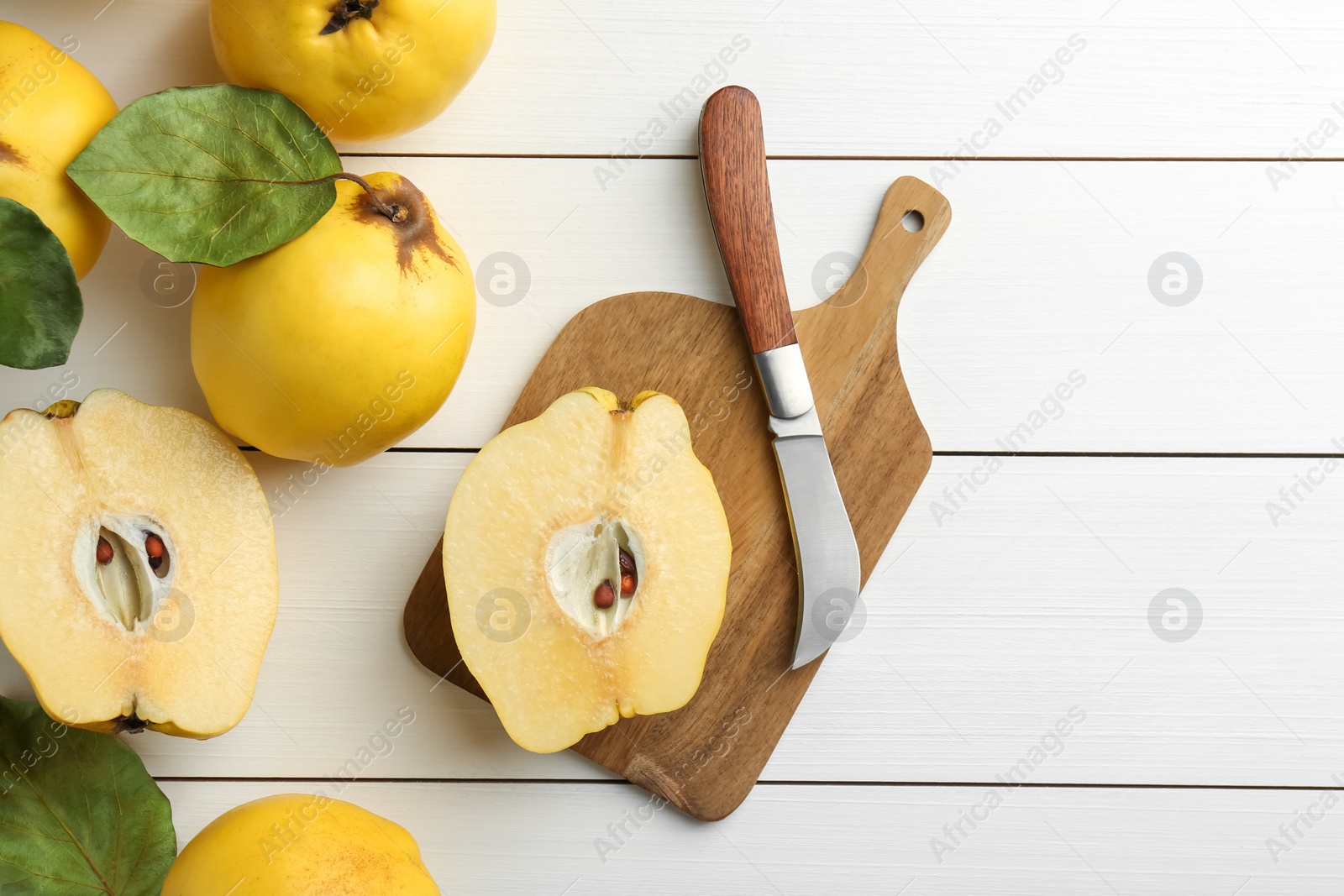 Photo of Tasty ripe quince fruits and knife on white wooden table, flat lay. Space for text