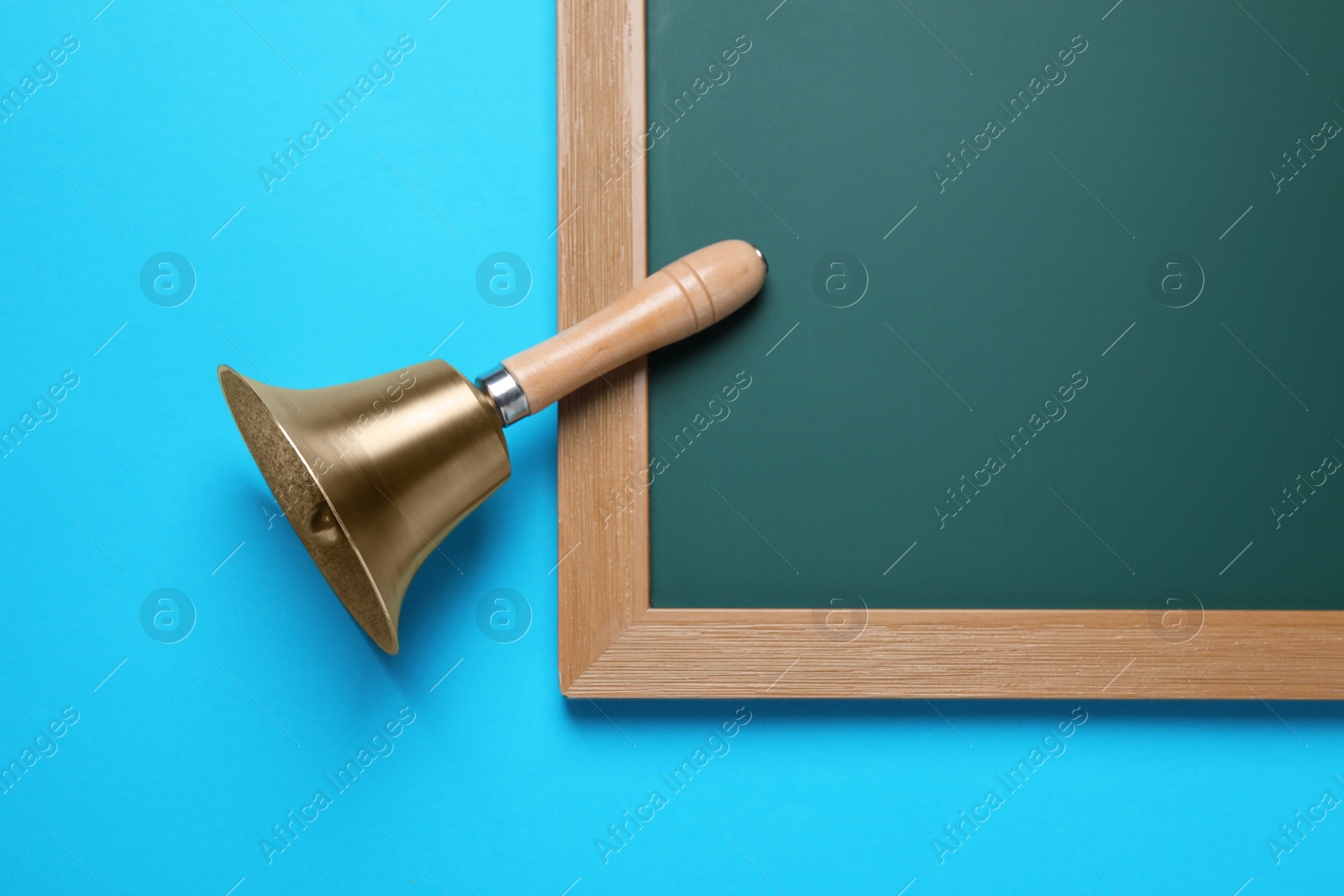 Photo of Golden bell and green chalkboard on light blue background, flat lay. School days