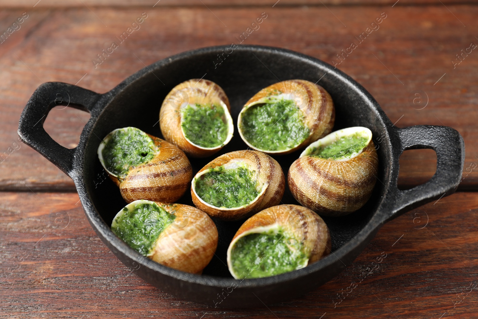 Photo of Delicious cooked snails in baking dish on wooden table, closeup