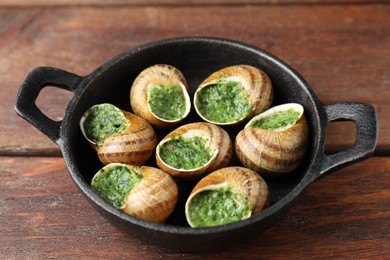 Delicious cooked snails in baking dish on wooden table, closeup