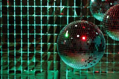 Photo of Shiny disco balls against foil party curtain under color lights, space for text