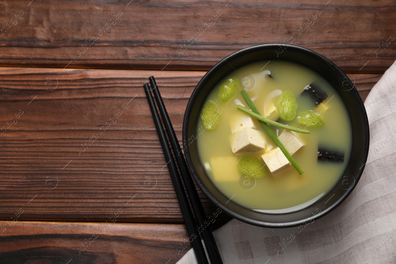 Photo of Bowl of delicious miso soup with tofu served on wooden table, top view. Space for text