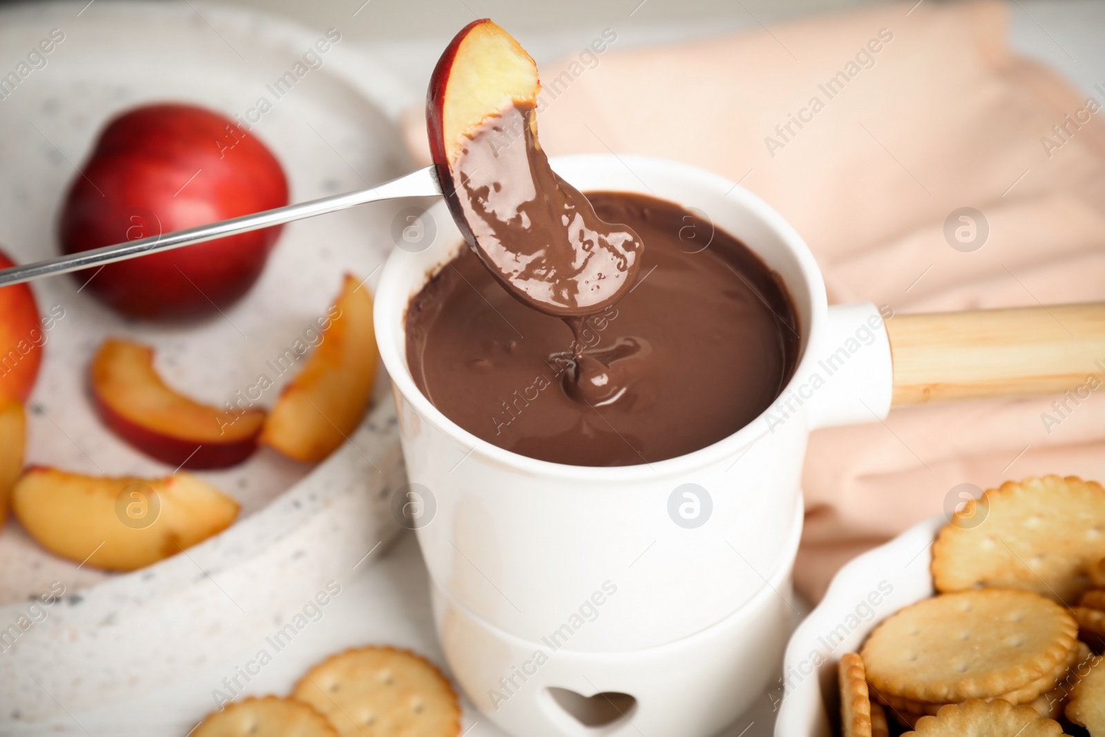 Photo of Fondue pot with chocolate and peach on table, closeup