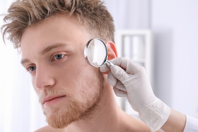 Photo of Dermatologist examining patient with magnifying glass in clinic, closeup view