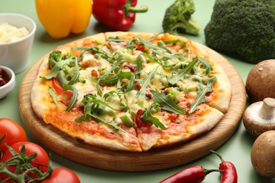 Photo of Delicious vegetarian pizza and products on green table, closeup