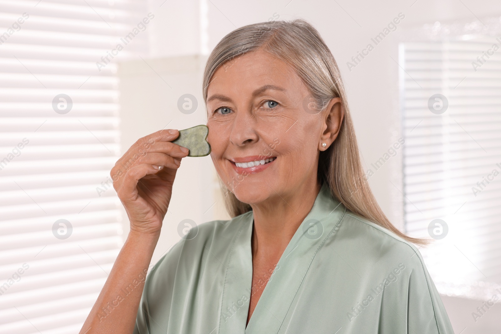 Photo of Woman massaging her face with jade gua sha tool in bathroom