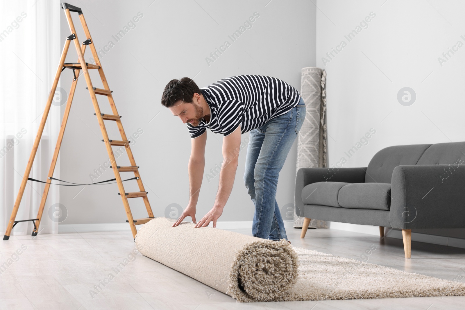 Photo of Man unrolling new clean carpet in room