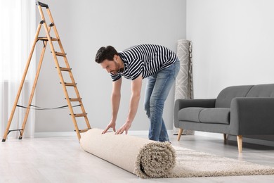 Photo of Man unrolling new clean carpet in room