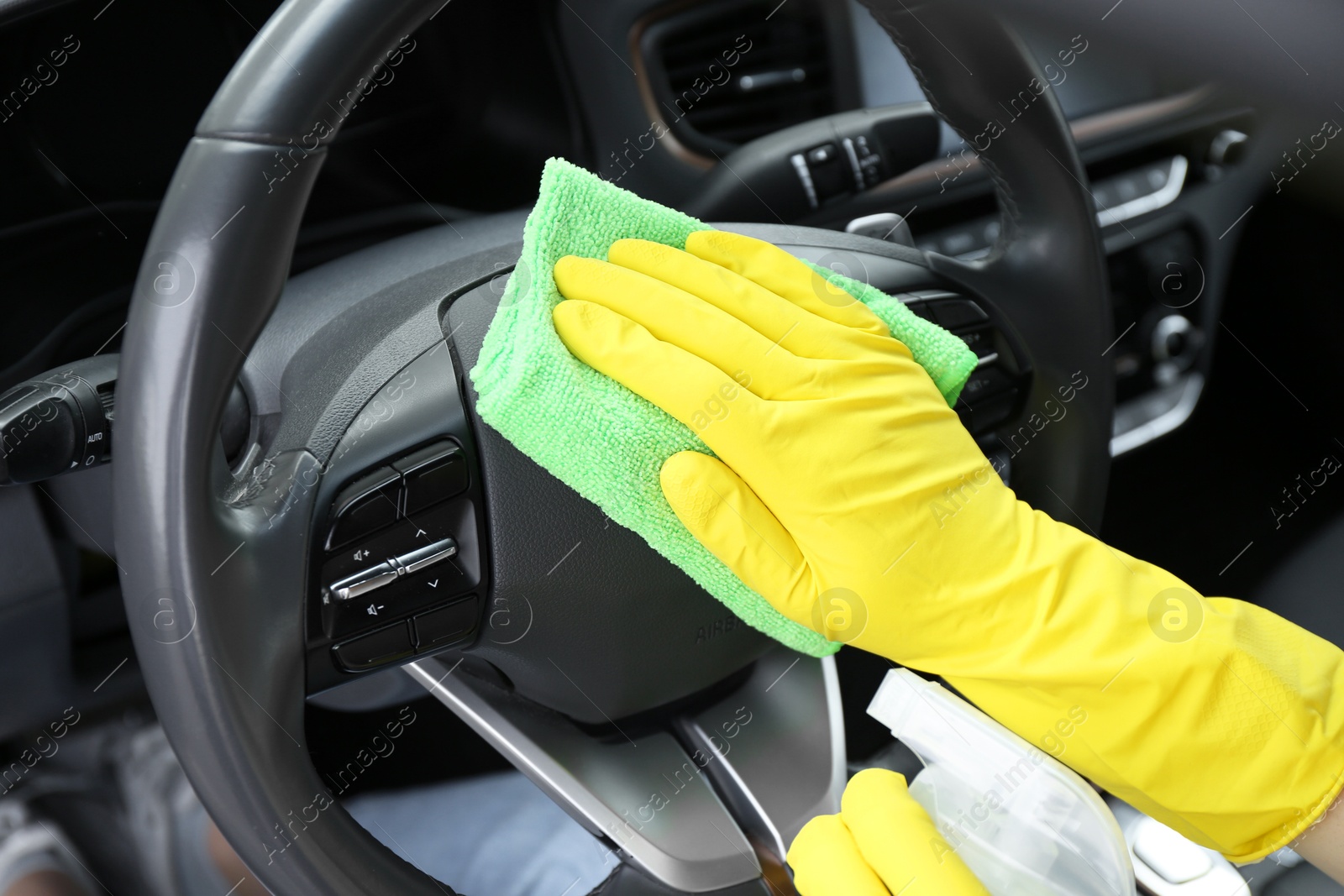 Photo of Woman cleaning steering wheel with rag in car, closeup