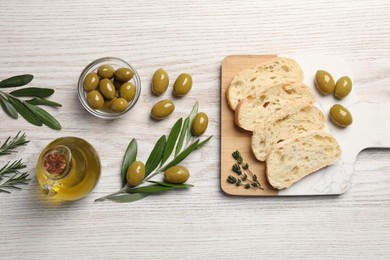 Photo of Cooking oil in jug, olives, herbs and ciabatta bread on wooden table, flat lay