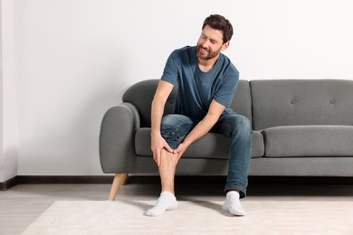 Man suffering from leg pain on sofa at home