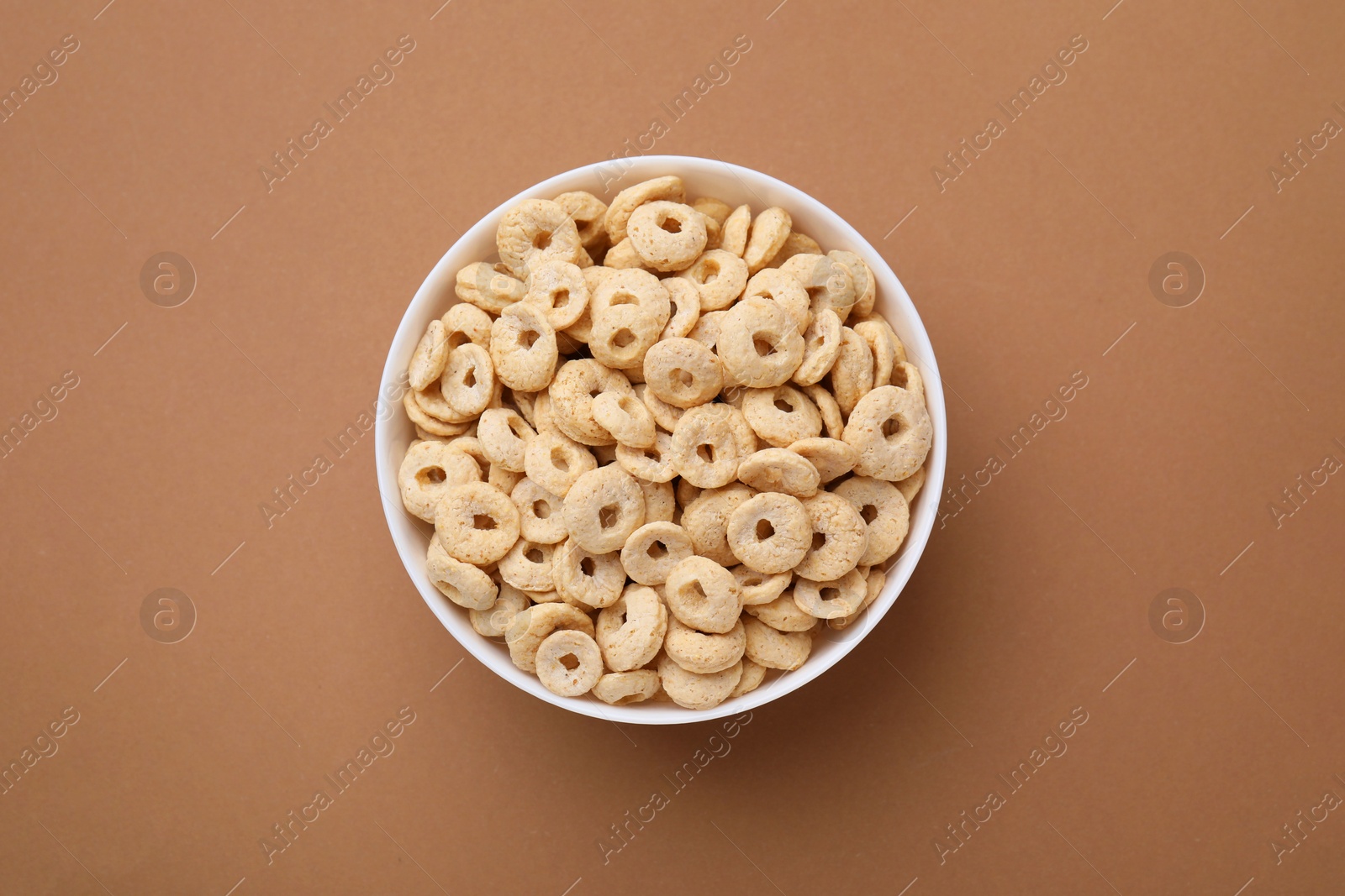 Photo of Tasty cereal rings in bowl on brown table, top view