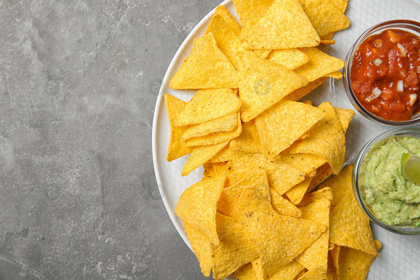 Photo of Plate with delicious mexican nachos chips and sauces on grey table, top view. Space for text