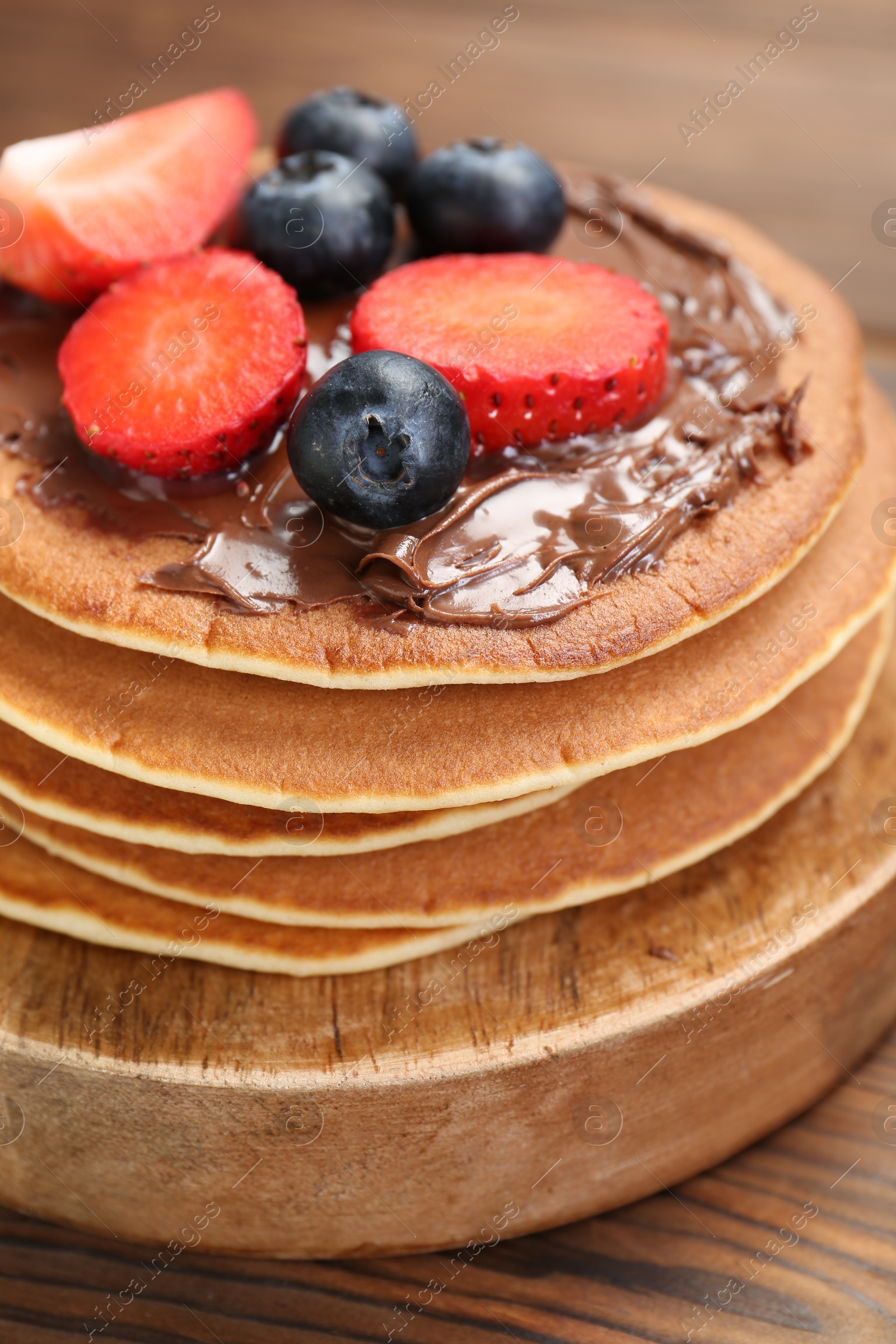 Photo of Tasty pancakes with chocolate paste and berries on wooden table, closeup