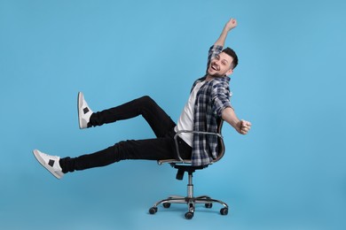 Photo of Excited man riding office chair on light blue background