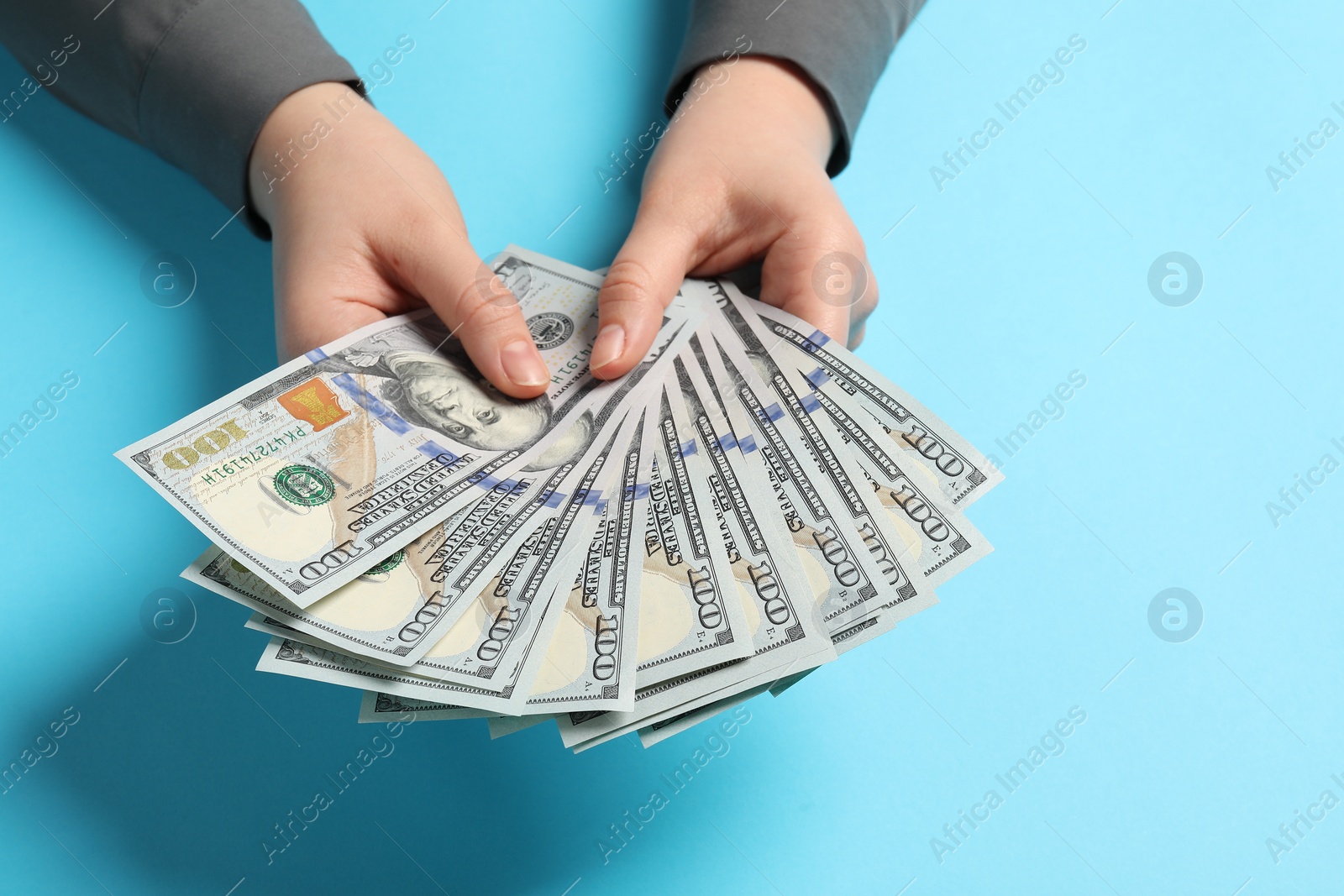 Photo of Money exchange. Woman holding dollar banknotes on light blue background, closeup