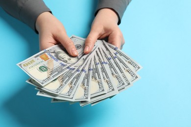 Photo of Money exchange. Woman holding dollar banknotes on light blue background, closeup