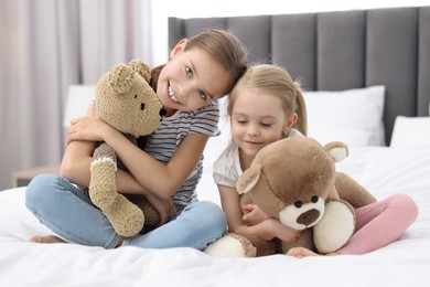 Cute little sisters with teddy bears on bed at home