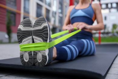 Photo of Woman doing exercise with fitness elastic band on mat outdoors, closeup