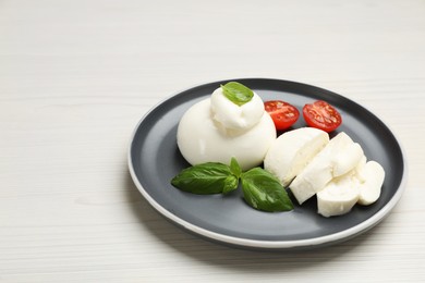 Photo of Delicious burrata cheese with basil and cut tomato on white wooden table