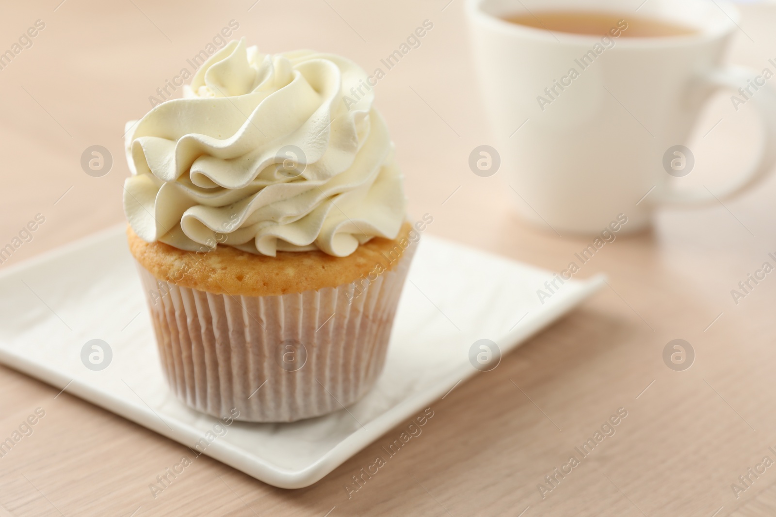 Photo of Tasty cupcake with vanilla cream on light wooden table, closeup