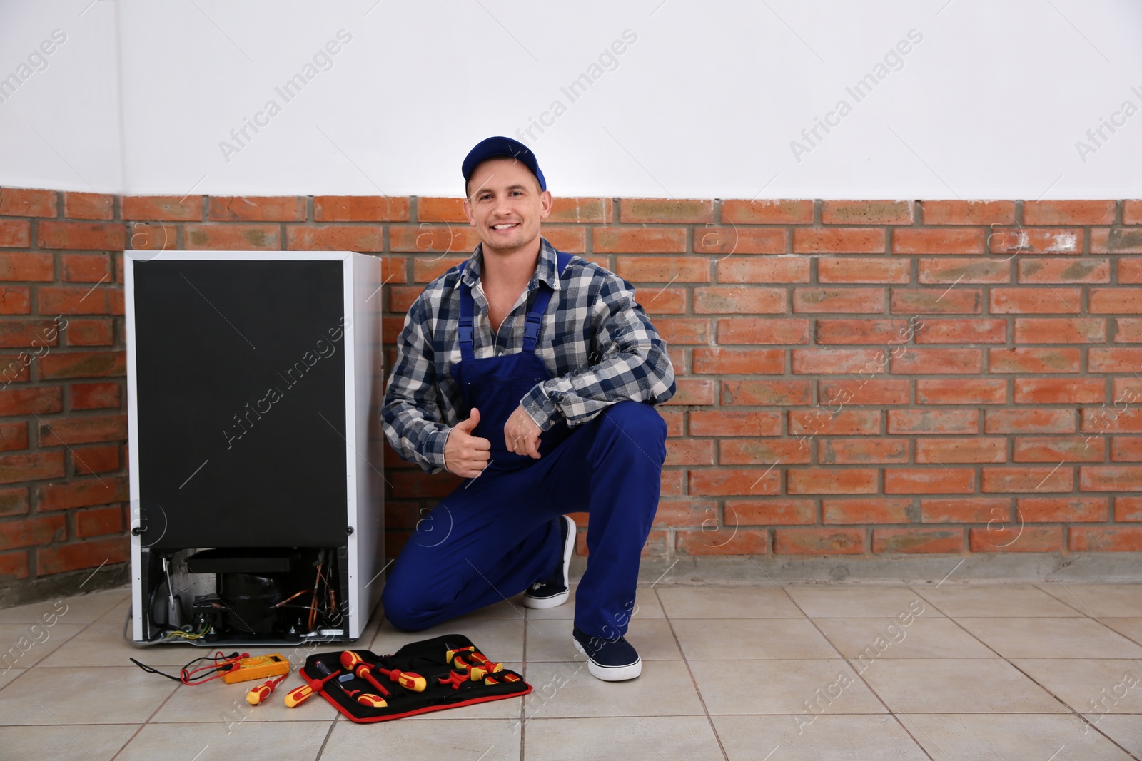 Photo of Male technician with tools near broken refrigerator indoors. Space for text