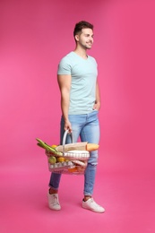 Photo of Young man with shopping basket full of products on pink background