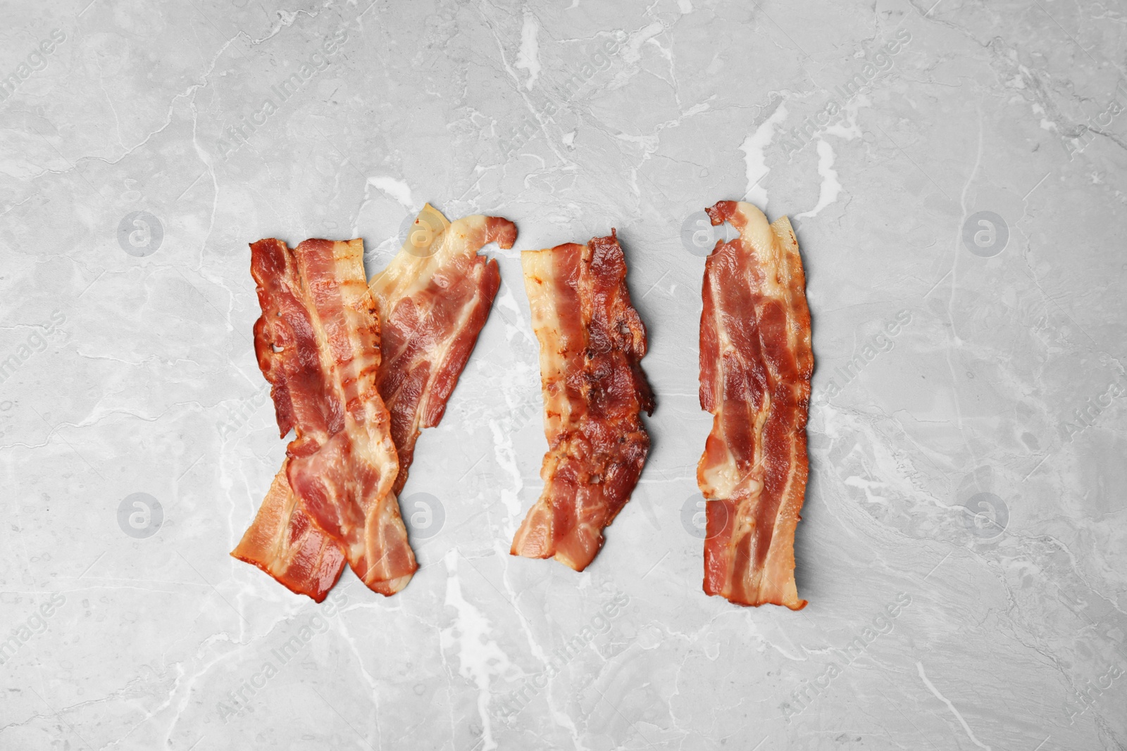 Photo of Slices of tasty fried bacon on light grey marble table, flat lay