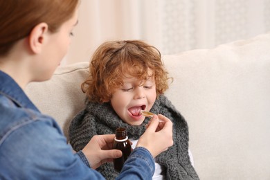 Photo of Mother giving cough syrup to her son on sofa indoors