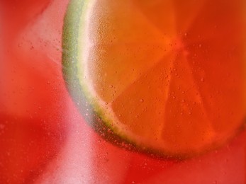 Glass of refreshing drink with ice cubes and lime slice as background, closeup