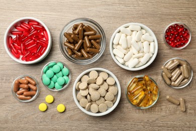 Different dietary supplements in bowls on wooden table, flat lay