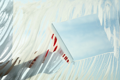 Photo of Woman cleaning window with squeegee on spring day, closeup